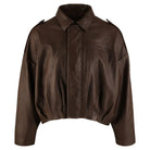 Die trueprodigy Feminine Lederjacke mit Hemdkragen und Raffung am Saum ist eine braune Schafslederjacke mit einer weiten, kastenförmigen Passform, langen Ärmeln, dezenten Schulterklappen, verdecktem Verschluss vorne und einem leicht eingeschnürten Saum.