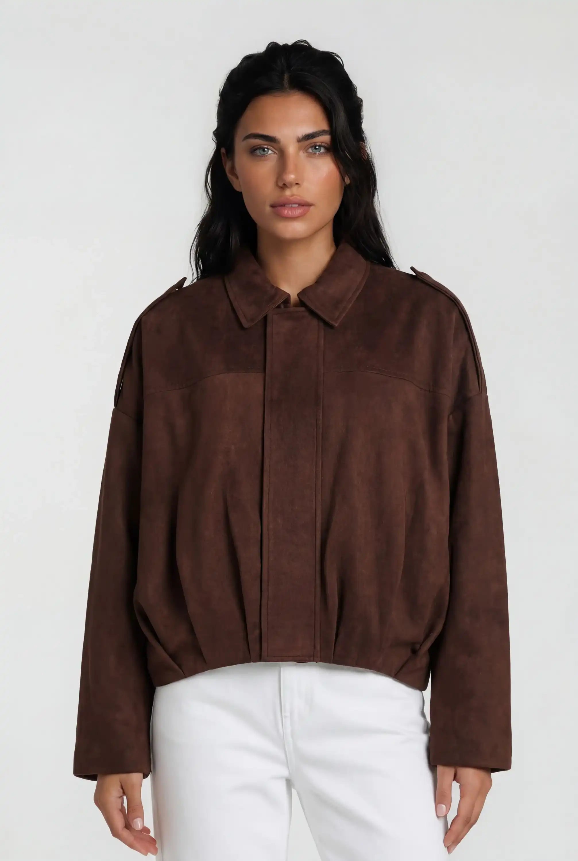 Eine Frau mit langen dunklen Haaren trägt die trueprodigy Clean-Cut Wildlederjacke Damen "Naeko" mit Hemdkragen und weißer Hose, steht vor einem schlichten hellen Hintergrund und blickt mit neutralem Gesichtsausdruck nach vorne.