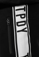 Nahaufnahme der trueprodigy Weston Sweathose mit Logoschrift in Schwarz mit stylischen Kontraststreifen, fettem TPDY-Schriftzug auf einer vertikalen weißen Platte und einer linken Tasche mit Reißverschluss.