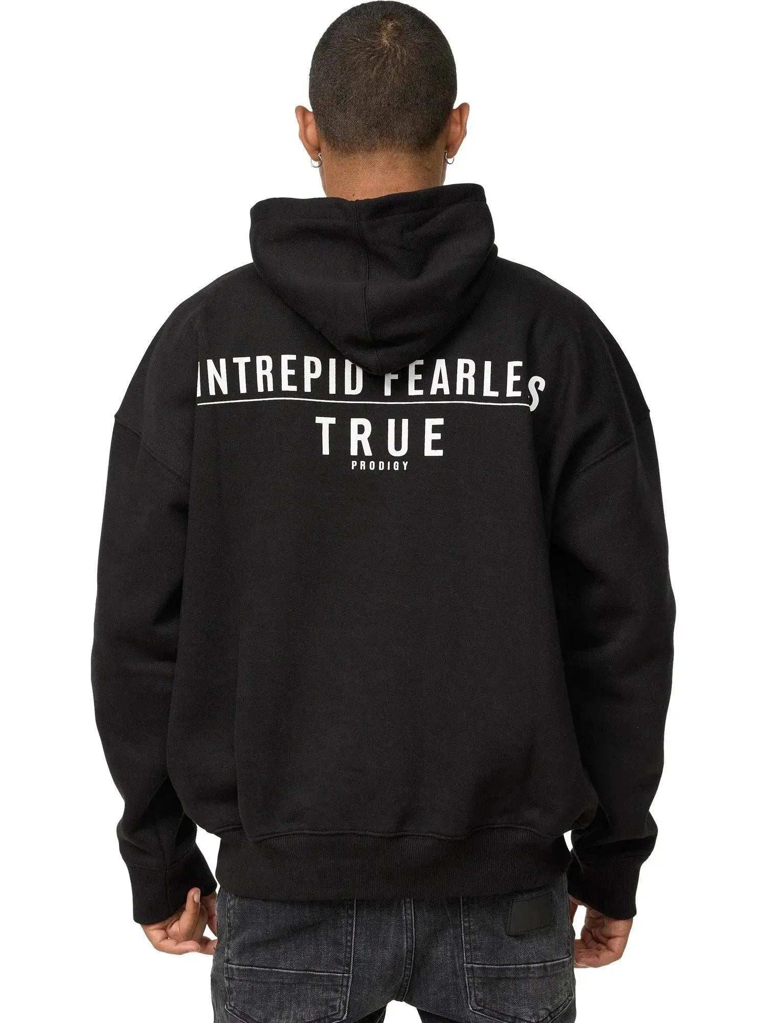 Eine Person mit kurzen Haaren ist von hinten zu sehen. Sie trägt den Aaren Oversized Hoodie mit Print von trueprodigy, auf dessen Rückseite „INTREPID FEARLESS TRUE PRODIGY“ in Weiß steht. Dazu tragen sie schwarze Jeans.