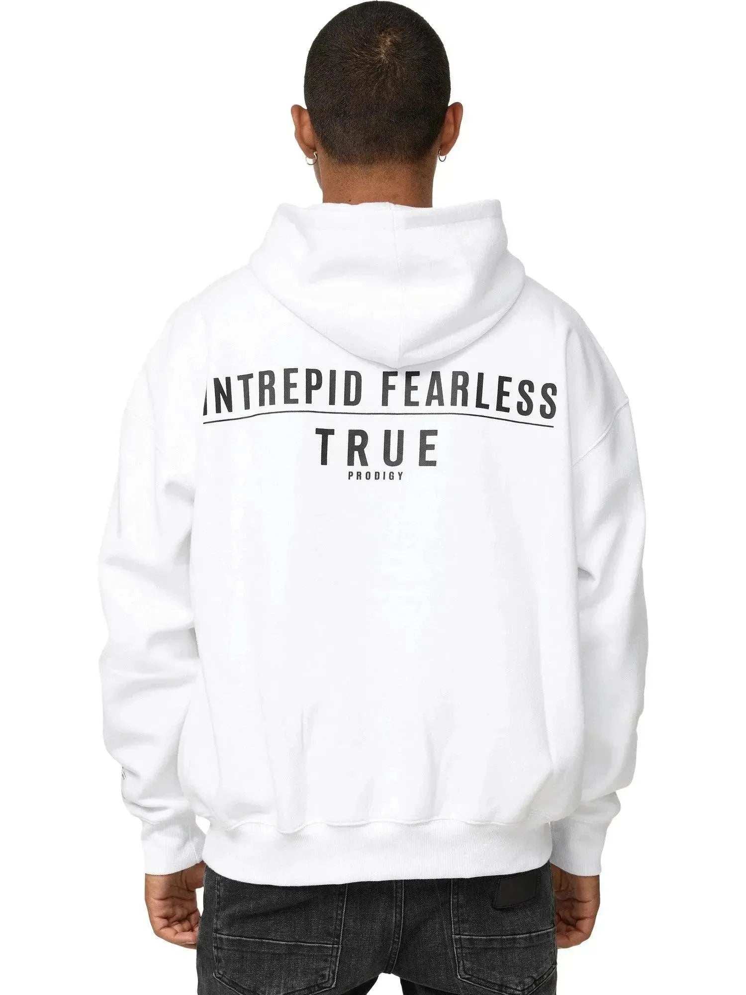 Eine Person steht mit dem Rücken zur Kamera vor einem weißen Hintergrund und trägt den übergroßen Unisex-Hoodie Aaren von trueprodigy. Dieser weiße Hoodie trägt in kräftigem Schwarz den Aufdruck „INTREPID FEARLESS TRUE PRODIGY“ und wird durch schwarze Jeans ergänzt.