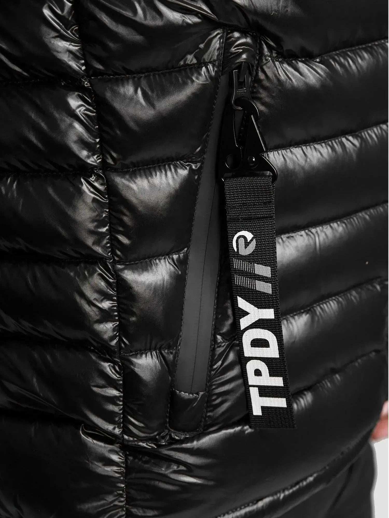 Nahaufnahme der schwarzen „Adan F Steppjacke mit Kapuze“ von trueprodigy, mit einer seitlichen Reißverschlusstasche mit „TPDY“-Anhänger. Der glänzende, wasserabweisende Stoff hat horizontale Nähte für Stil und Funktion.