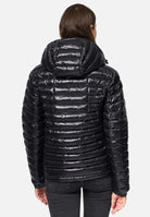 Eine Person trägt die Steppjacke mit Kapuze von trueprodigy Adan F, eine schwarze, glänzende Steppjacke mit horizontalen Nähten. Mit dem Rücken zur Kamera kombiniert sie dunkle Jeans vor einem schlichten weißen Hintergrund.
