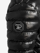 Nahaufnahme der Adan F Steppjacke mit Kapuze von trueprodigy. Sie verfügt über eine glänzende, wasserabweisende Oberfläche mit einem schwarzen Patch mit weißer Schrift in achteckiger Form, der Stil und Funktionalität in dieser trendigen Damenjacke vereint.