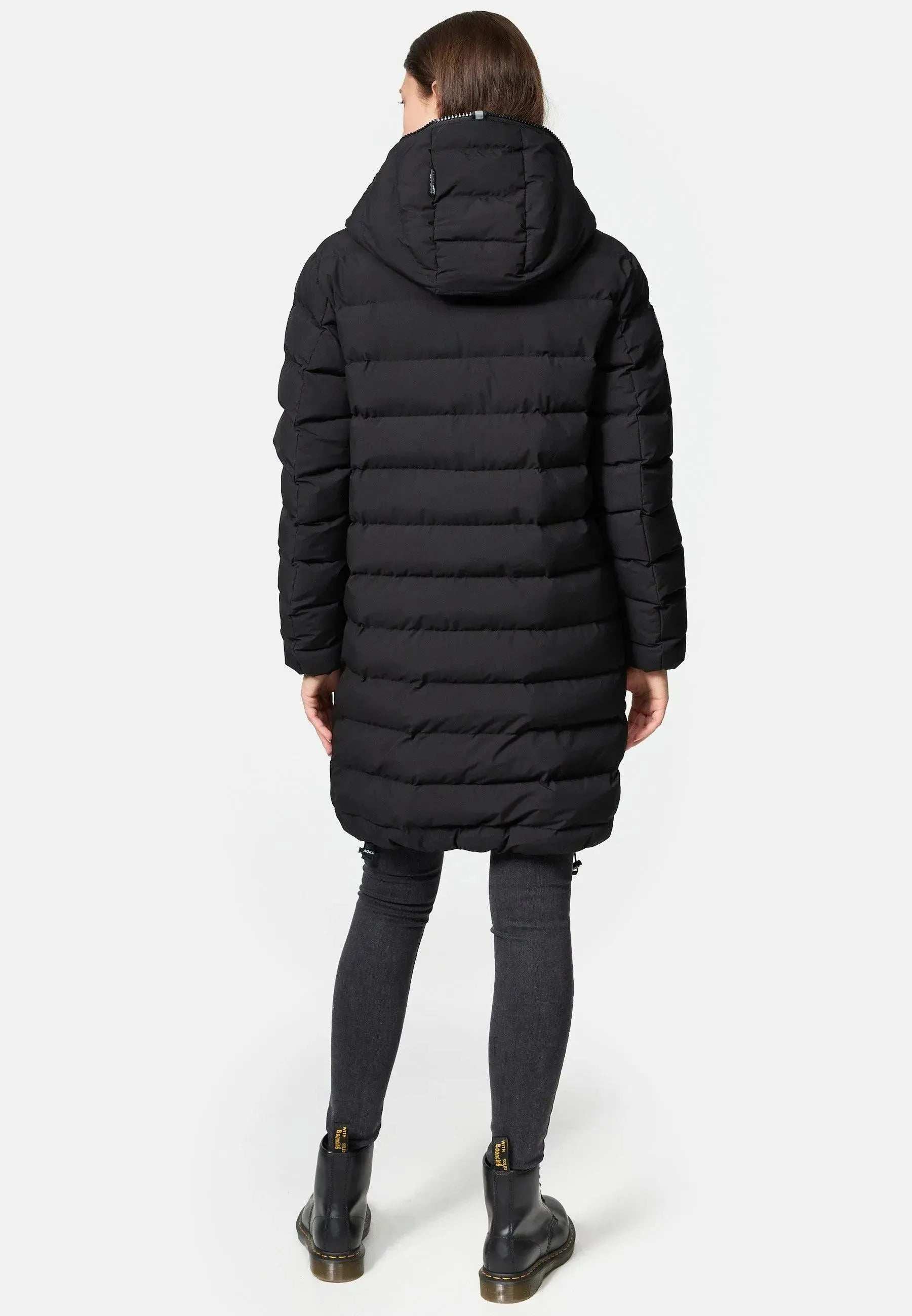 Eine Figur steht mit abgewandtem Gesicht in einer Chester F Lange Pufferjacke mit Logo von trueprodigy. Die lange schwarze Pufferjacke besteht aus wasserabweisendem Material und hat einen Reißverschluss, der Licht einfängt. Sie trägt sie mit dunkelgrauen Röhrenjeans und schwarzen Stiefeletten auf einem schlichten weißen Hintergrund.