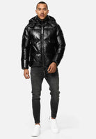TRUEPRODIGY constance schwarze Pufferjacke, glänzendes Material, Kapuze, Schriftzug TPDY, getragen von Mann in Jeans und weißen Sneakern, modischer Winterstil, perfekte urbane Outdoor-Bekleidung.