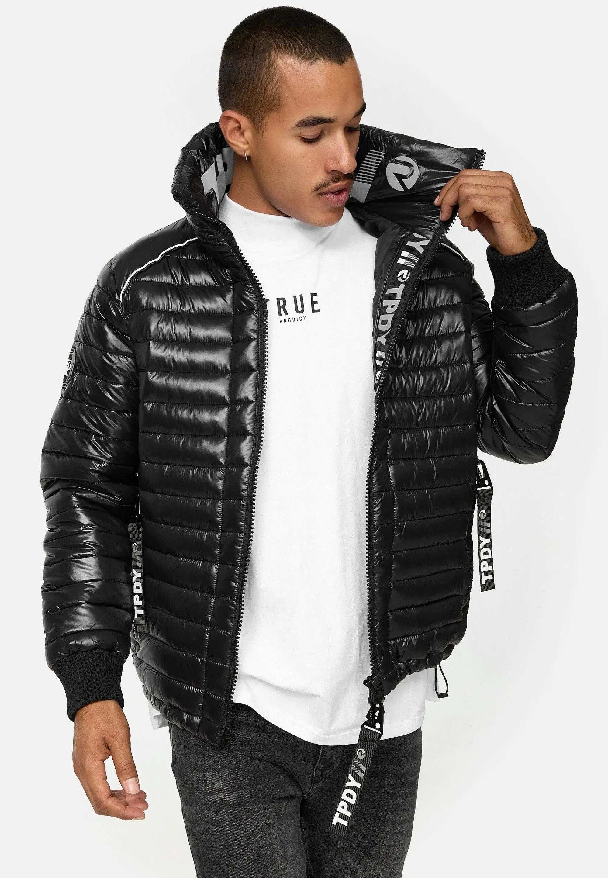 Eine Person mit kurzen Haaren steht vor einem schlichten weißen Hintergrund und passt den Reißverschluss ihrer Corey Steppjacke mit Stehkragen von trueprodigy an. Sie trägt eine glänzende schwarze Pufferjacke über einem weißen T-Shirt mit Trägern mit TPOY-Logo.