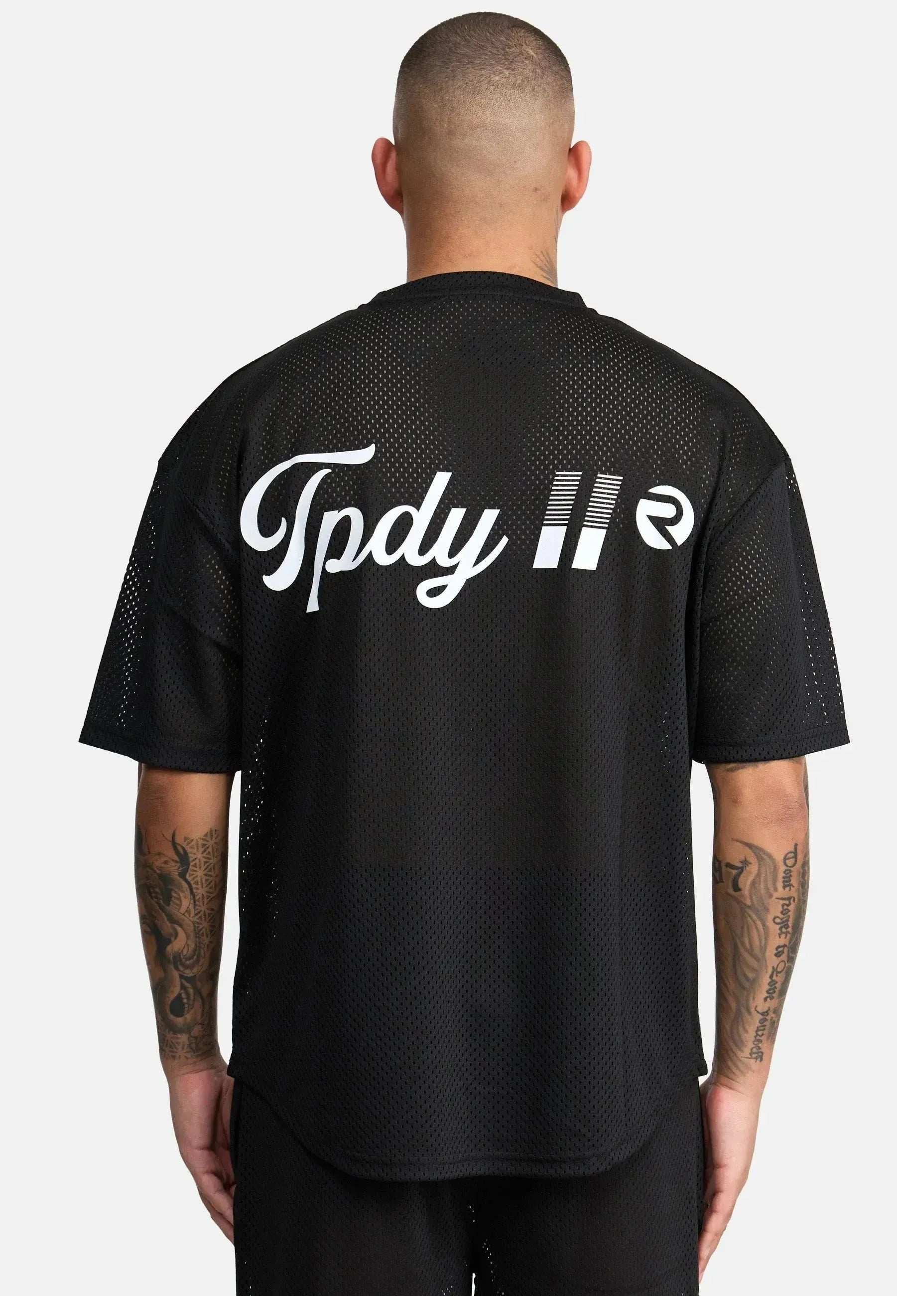 Eine Person mit kurzen Haaren und sichtbaren Armtattoos blickt von der Kamera weg und trägt das Trueprodigy Daniel Oversized T-Shirt mit Druck. Das schwarze Mesh-T-Shirt trägt den weißen „Tpdy 11“-Text und ein kleines Logo und verströmt Vintage-Vibes.