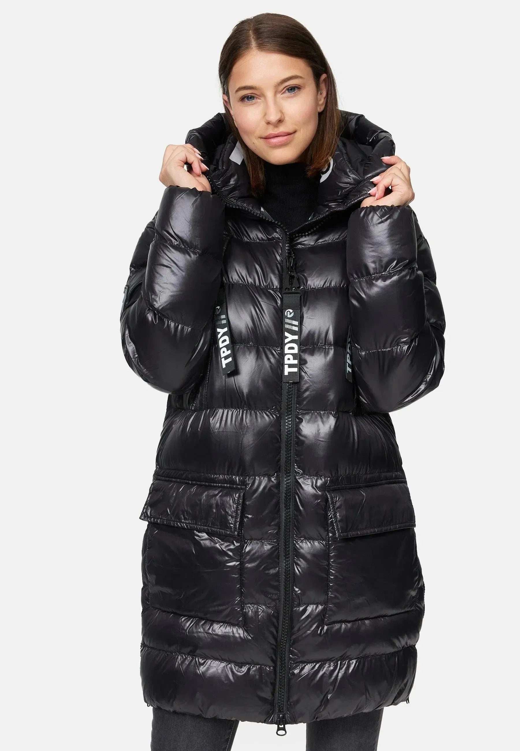 Eine Person trägt die David F Glänzende Steppjacke mit Kapuze von trueprodigy. Die lange schwarze Steppjacke in glänzender Optik hat große Vordertaschen und einen vertikalen Reißverschluss. Die Person steht vor einem schlichten weißen Hintergrund und hält die Kapuze mit beiden Händen.