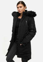Eine Person trägt einen trueprodigy Harvey F Damenparka mit Kapuze und Kunstfell vor einem schlichten weißen Hintergrund. Der Mantel mit mehreren Taschen passt perfekt zu ihrer schwarzen Hose und ihrem Oberteil, während sie ihre Hände lässig in die Taschen steckt.