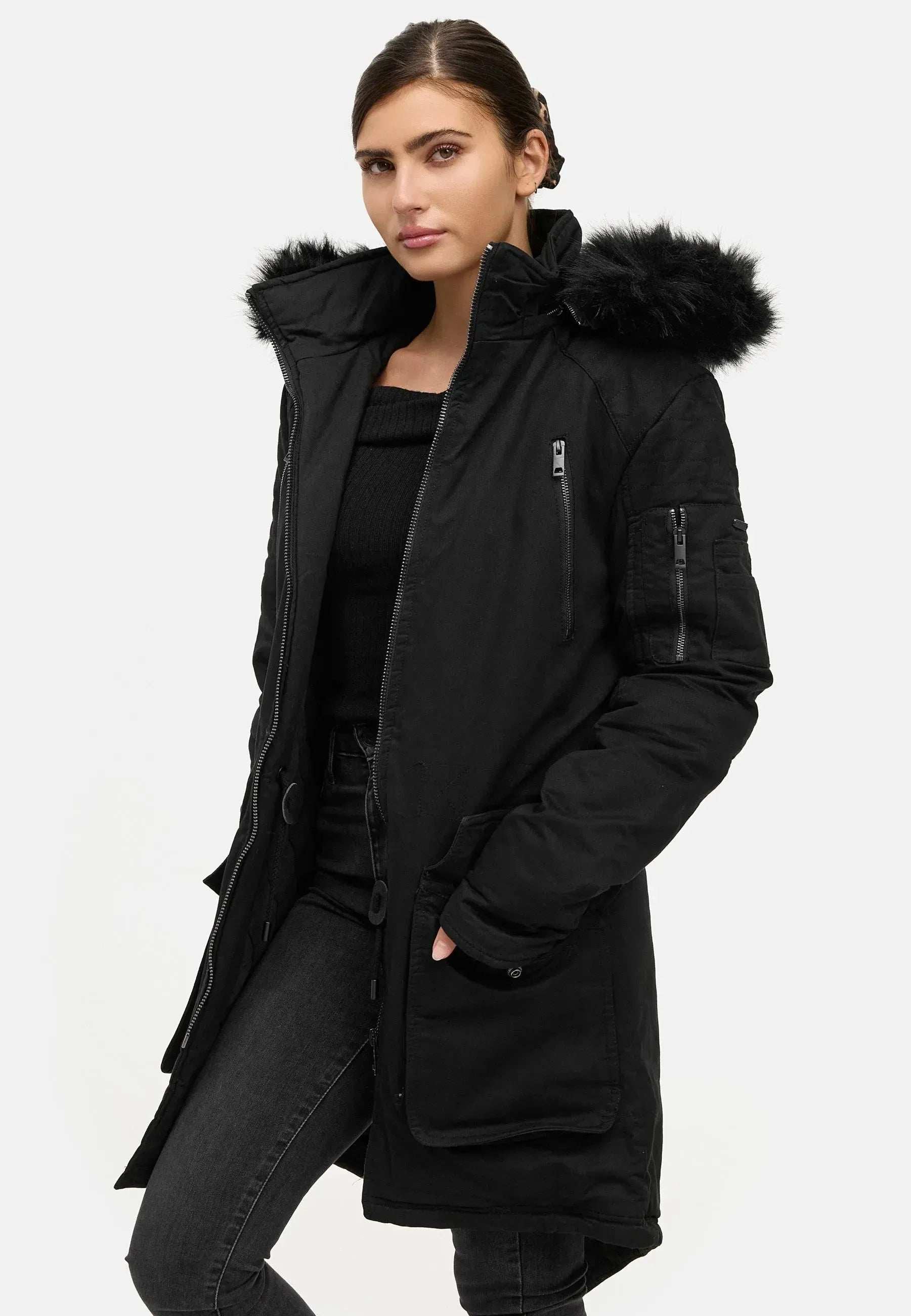 Eine Person trägt einen trueprodigy Harvey F Damenparka mit Kapuze und Kunstfell vor einem schlichten weißen Hintergrund. Der Mantel mit mehreren Taschen passt perfekt zu ihrer schwarzen Hose und ihrem Oberteil, während sie ihre Hände lässig in die Taschen steckt.