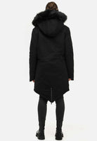 Rückansicht einer Person, die einen Damenparka mit Kapuze und Kunstfell von trueprodigy Harvey F trägt, der ein langes, leicht verjüngtes Design aufweist. Sie kombinieren ihn mit dunklen Hosen und schwarzen Stiefeln, alles vor einem schlichten weißen Hintergrund.