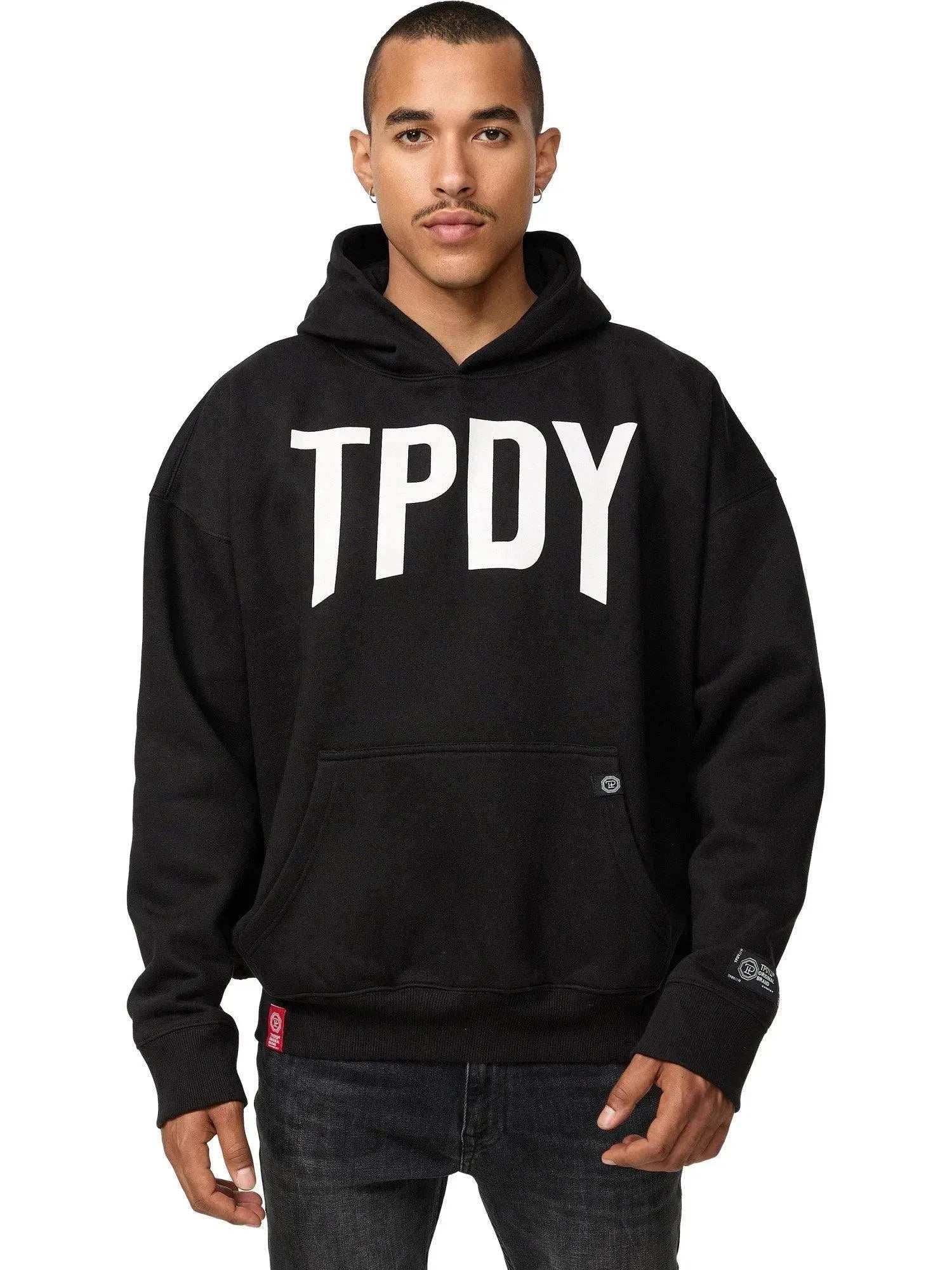Vor einem schlichten weißen Hintergrund steht jemand im Trueprodigy Janne Oversized Hoodie mit Print – mit „TPDY“ in Weiß – stilvoll da. Die kurzen Haare und der neutrale Ausdruck verstärken die allgemeine Coolness dieses Unisex-Kapuzensweatshirts.