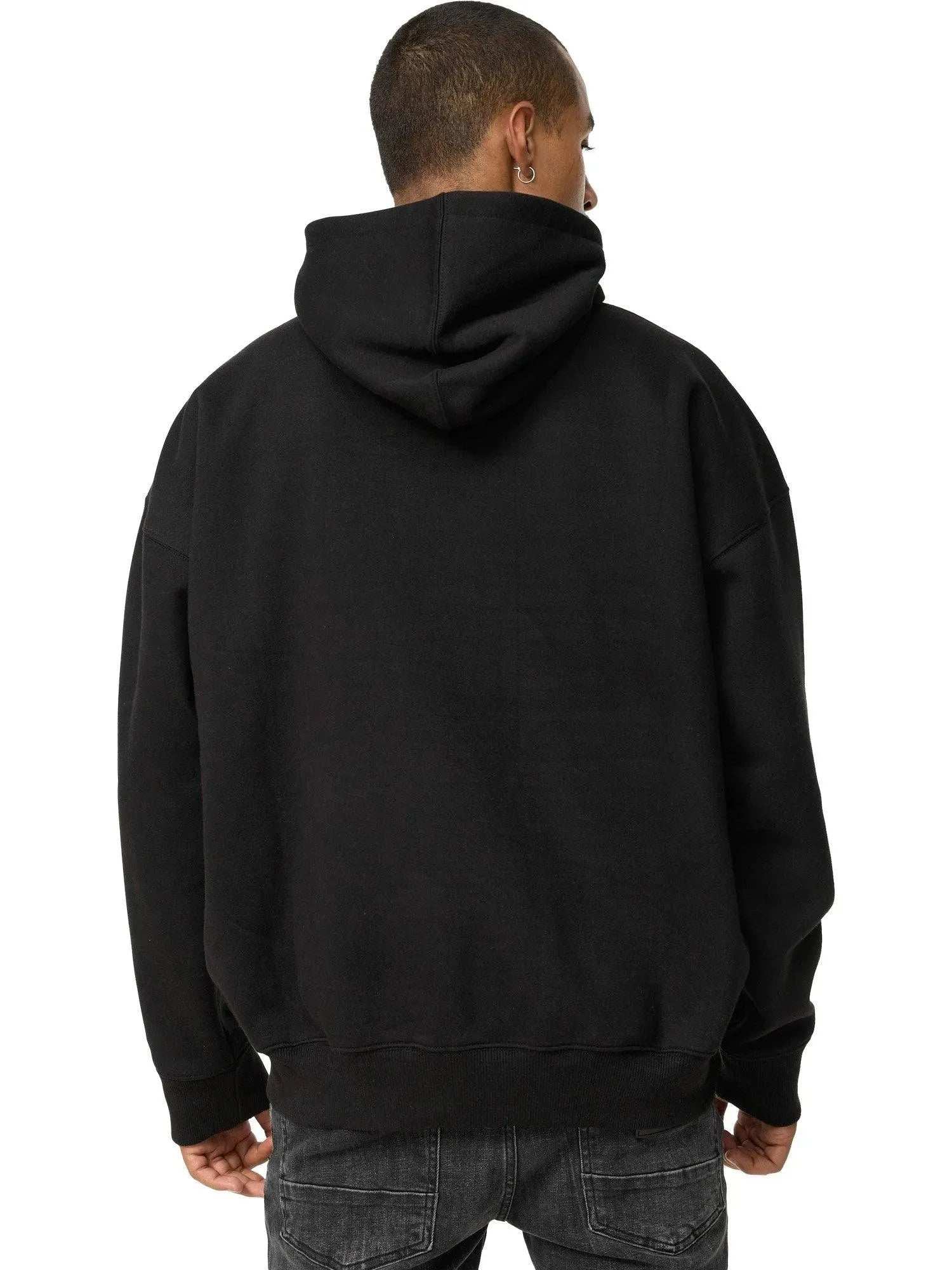 Jemand, der einen schwarzen Janne Oversized Hoodie mit Print und dunkle Jeans trägt, ist von hinten zu sehen, mit heruntergelassener Kapuze, wodurch das Trueprodigy-Logo dezent vor einem weißen Hintergrund zu sehen ist.