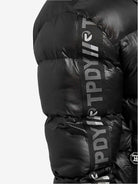 Nahaufnahme einer bauschigen schwarzen Logan Pufferjacke mit Logo von trueprodigy, mit „TPDY“-Text und Logo auf dem Ärmel. Diese wattierte Jacke hat glänzenden, gesteppten Stoff für Wärme und die Logan-Silhouette bietet einen eleganten Look vor einem schlichten weißen Hintergrund.