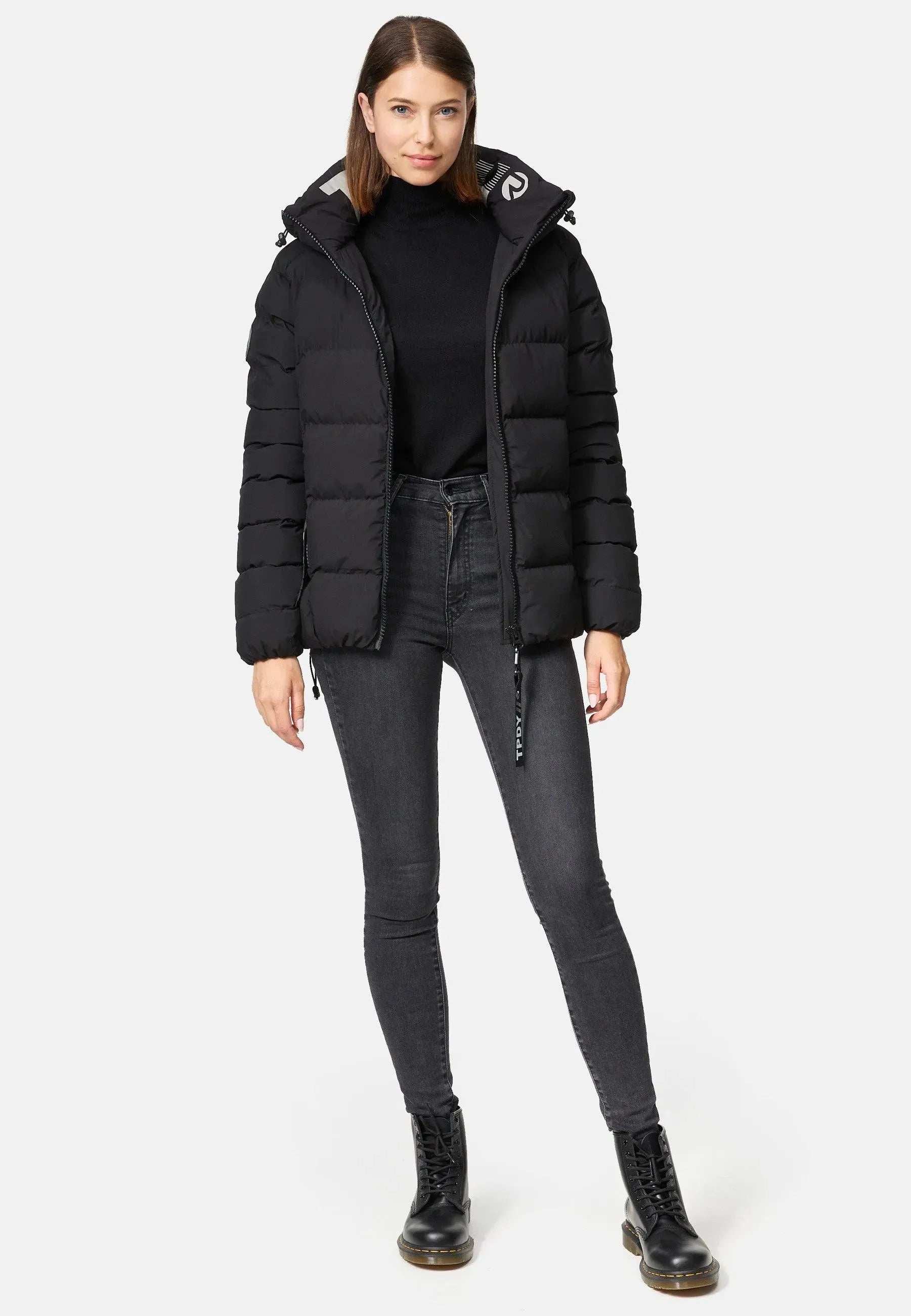 Vor einem weißen Hintergrund trägt jemand eine Trueprodigy Murphy F Matte Steppjacke mit Kapuze, einen schwarzen Rollkragenpullover, dunkelgraue Röhrenjeans und schwarze Stiefel. Die Hände sind in den Taschen und der Blick ist nach vorne gerichtet.