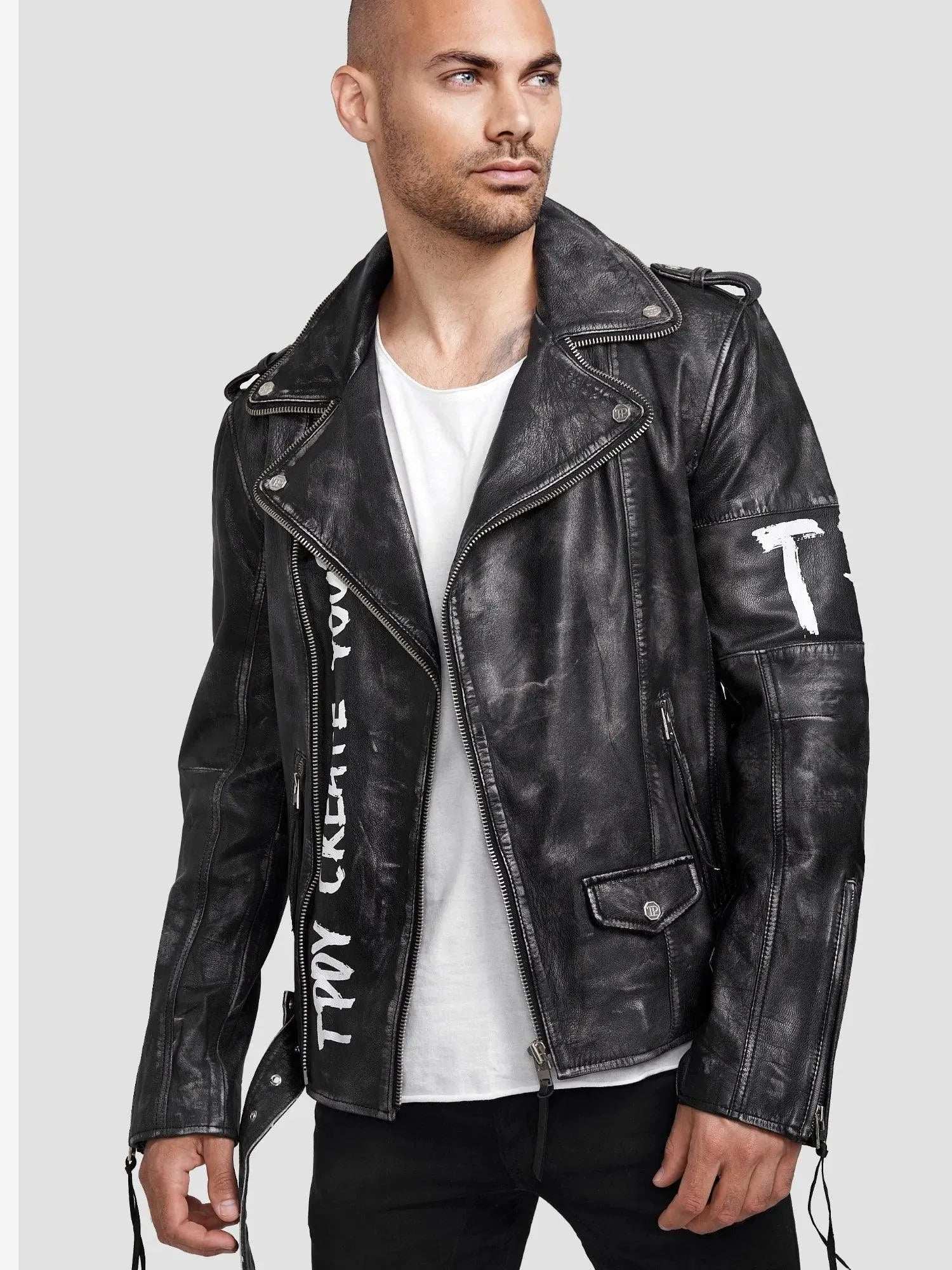 Eine Person trägt die Russell Lederjacke mit Print von trueprodigy, mit Nieten, silbernen Reißverschlüssen und sichtbaren Nähten für einen klassischen Biker-Look. Das Ensemble besteht aus einem weißen T-Shirt und einer schwarzen Hose vor einem schlichten hellgrauen Hintergrund.