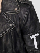 Nahaufnahme der Russell Lederjacke mit Print von trueprodigy mit silbernen Reißverschlüssen, Metallknöpfen und klassischem Biker-Look. Auf den Ärmel ist ein weißes „T“ mit sichtbarem Patchwork und Struktur aufgemalt, und eine Schulterklappe vervollständigt das kantige Design.